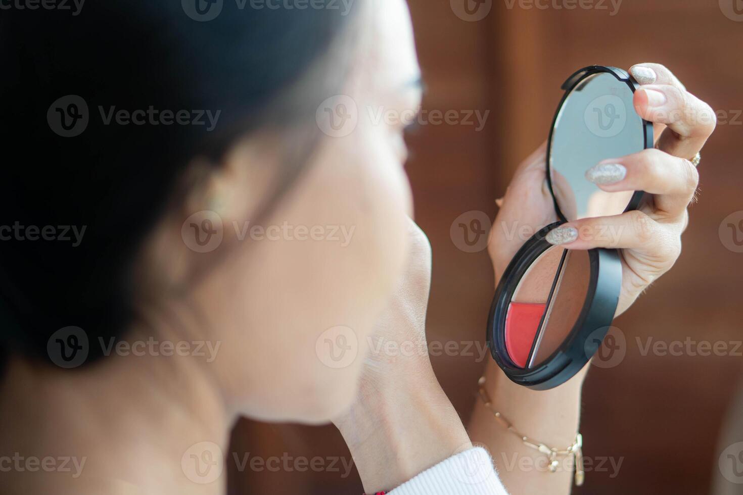 Woman applying makeup with a compact mirror photo