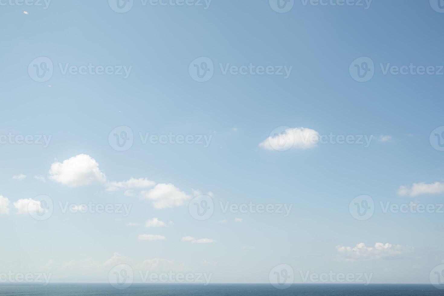 Clear blue sky with scattered clouds over calm ocean photo