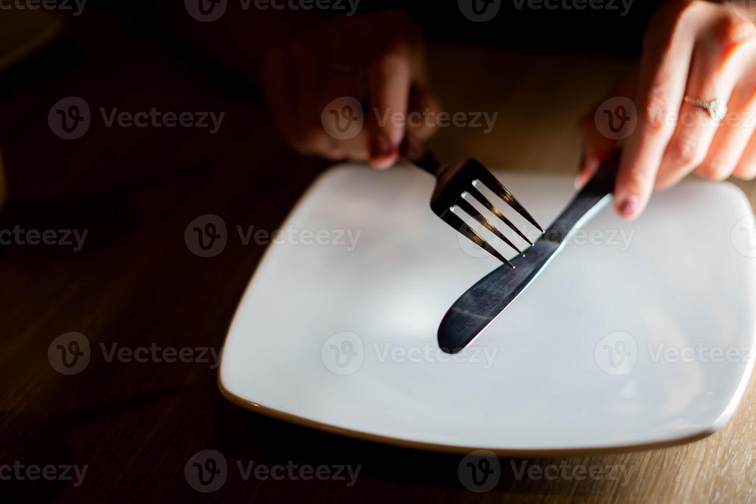 Person holding fork and knife over empty plate photo