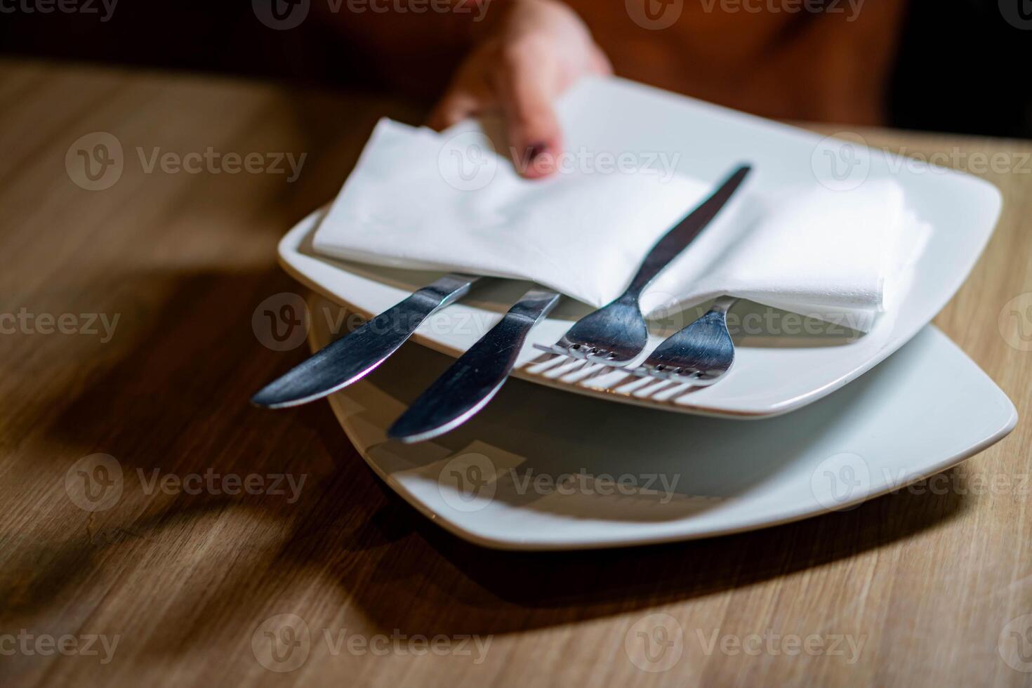 Hand placing stacked plates with cutlery on table photo