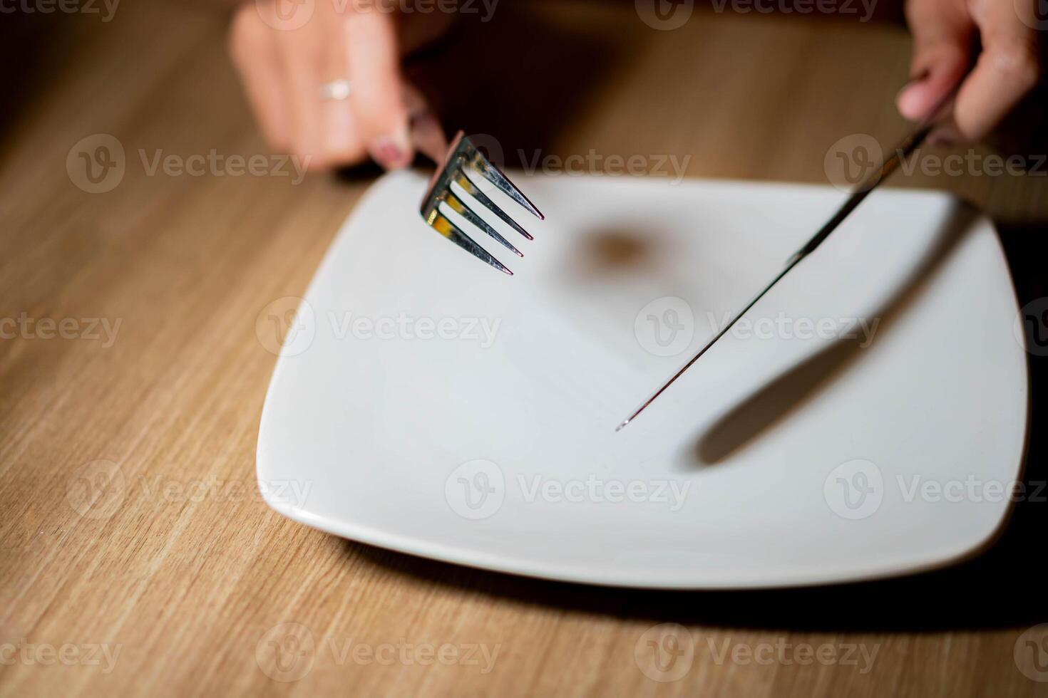 Person holding fork and knife over empty plate photo