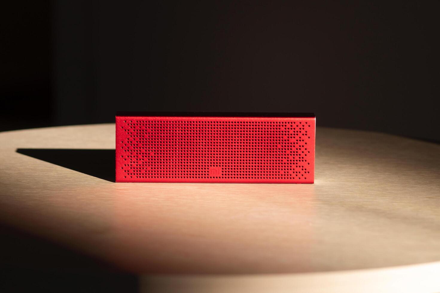 Poznan, Poland - 10.20.2022 Xiaomi Mi Bluetooth Speaker Portable red music speaker located on a wooden table in the rays of the sun photo