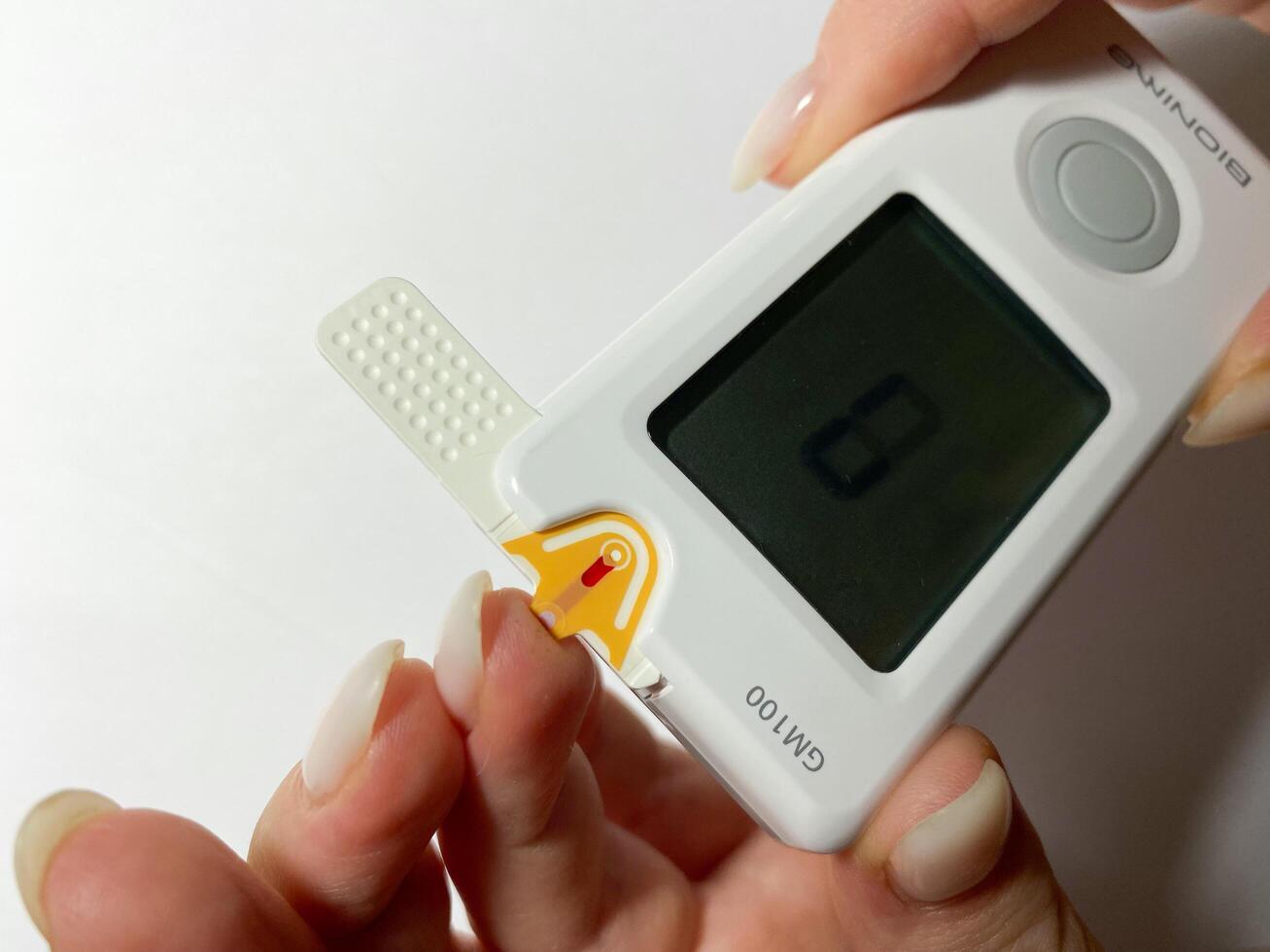 Warsaw, Poland - 09.19.2021 Measurement of blood sugar using a Bionime glucose meter. Piercing a finger to take blood photo