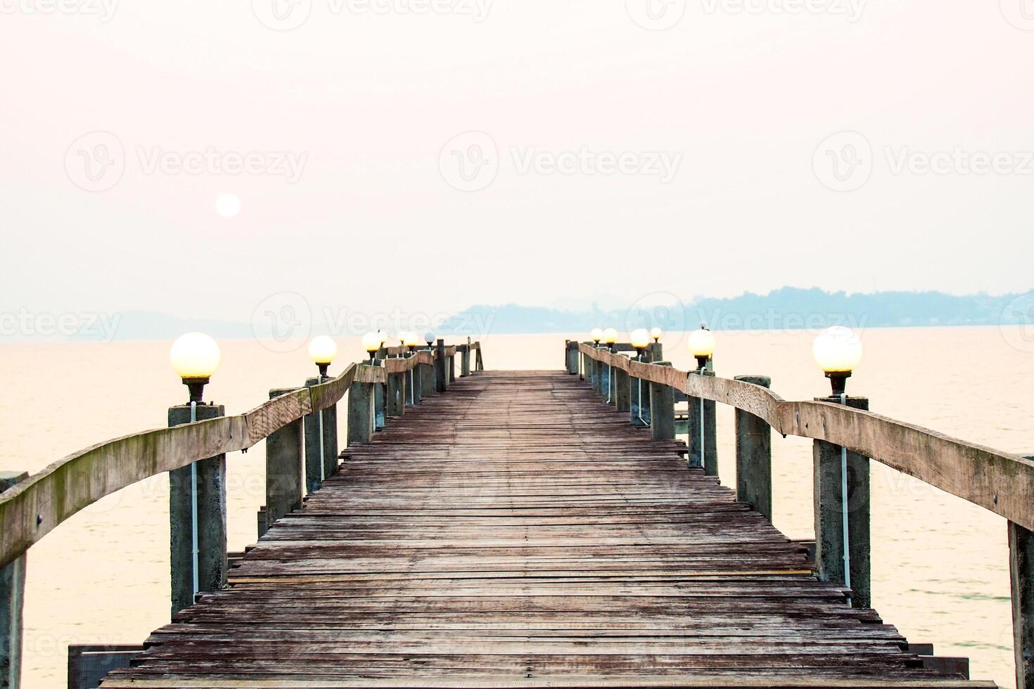 Serene Wooden Pier Extending into Calm Sea at Sunset with Soft Lighting and Distant Hills photo