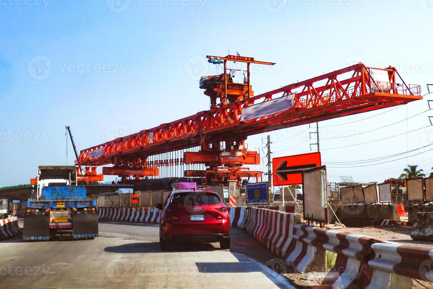 Large Red Construction Crane on Highway with Vehicles and Safety Barriers Under Clear Blue Sky photo