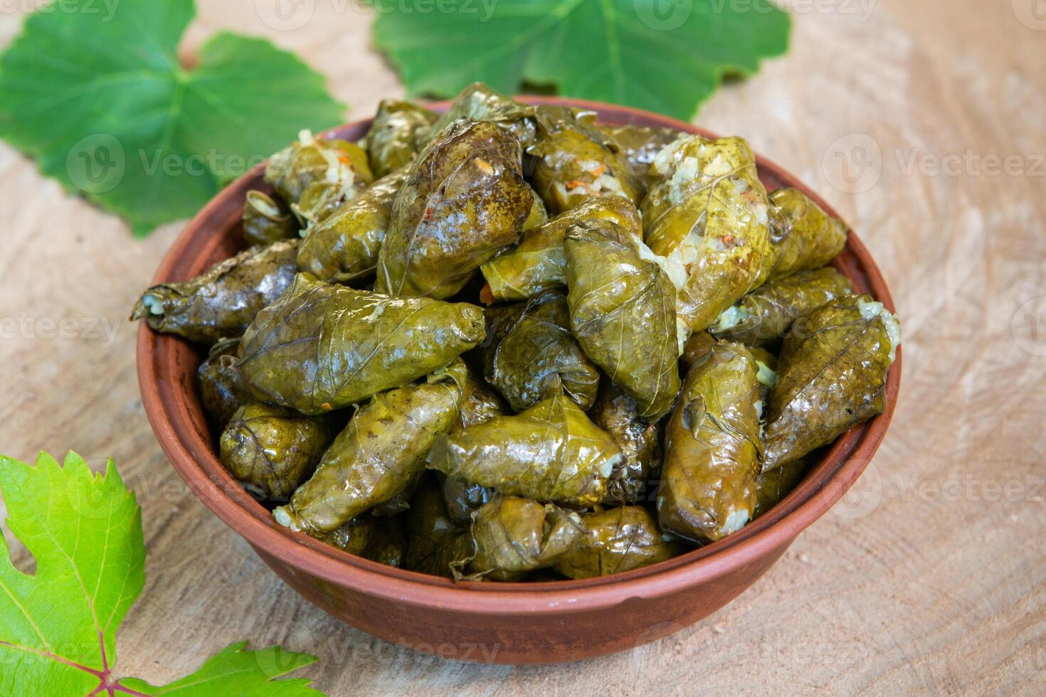 Dolma a stuffed grape leaves in a clay bowl on wooden background photo