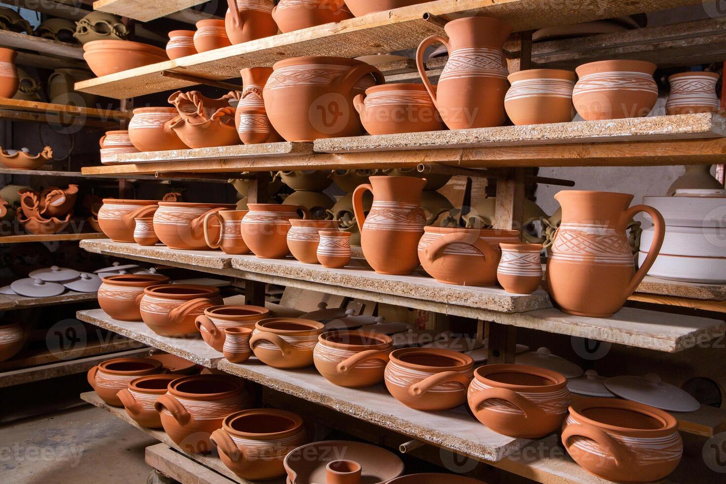 Freshly made clay mugs, pots and bowls drying up on wooden shelves in pottery workshop. Handmade ceramics manufacture. Different clay pots in workshop. photo