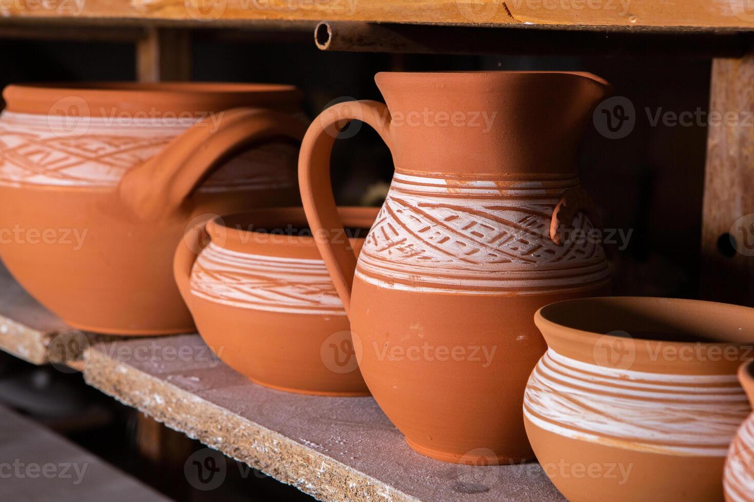 Freshly made clay mugs, pots and bowls drying up on wooden shelves in pottery workshop. Handmade ceramics manufacture. Different clay pots in workshop. photo