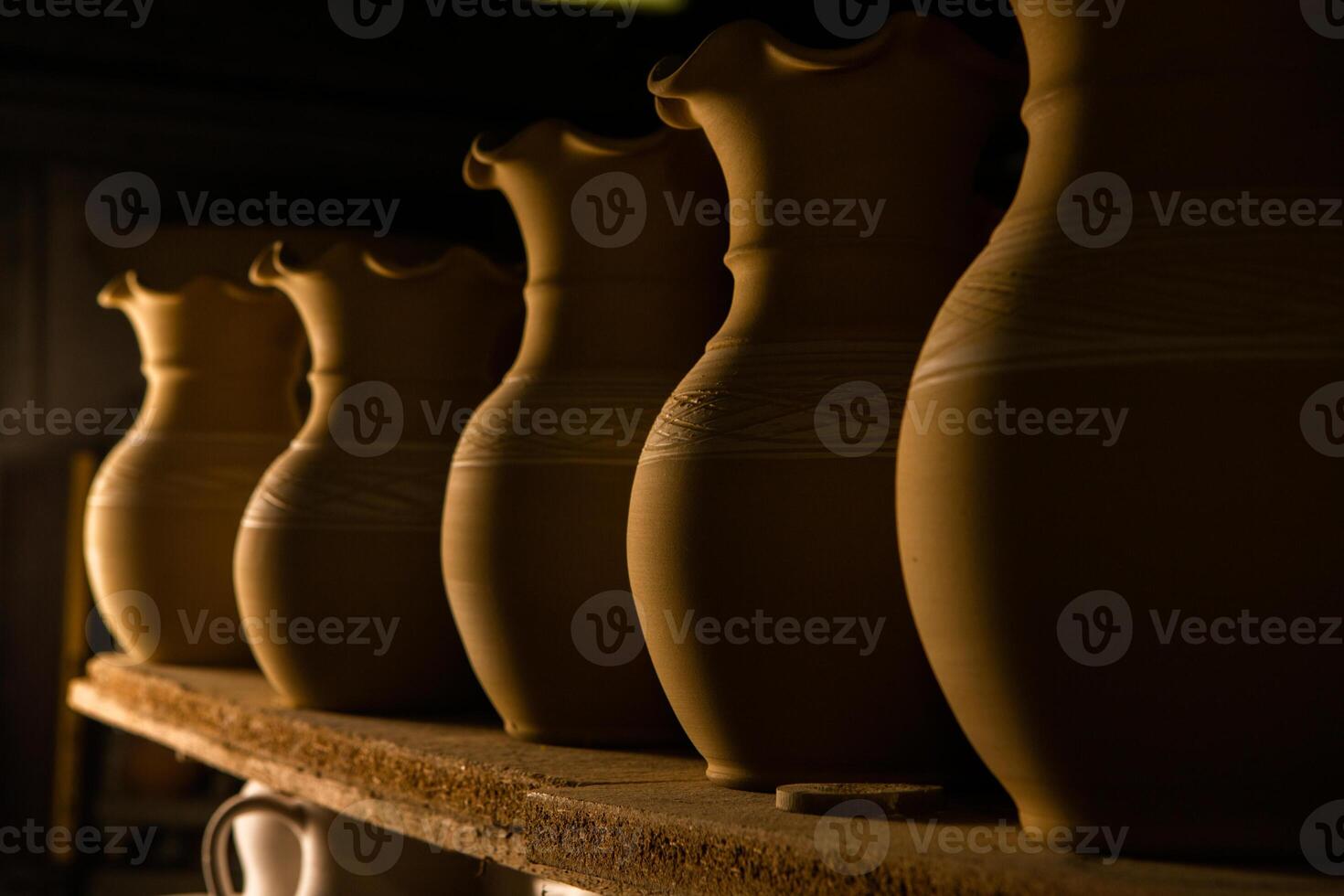 Freshly made clay mugs, pots and bowls drying up on wooden shelves in pottery workshop. Handmade ceramics manufacture. Different clay pots in workshop. photo