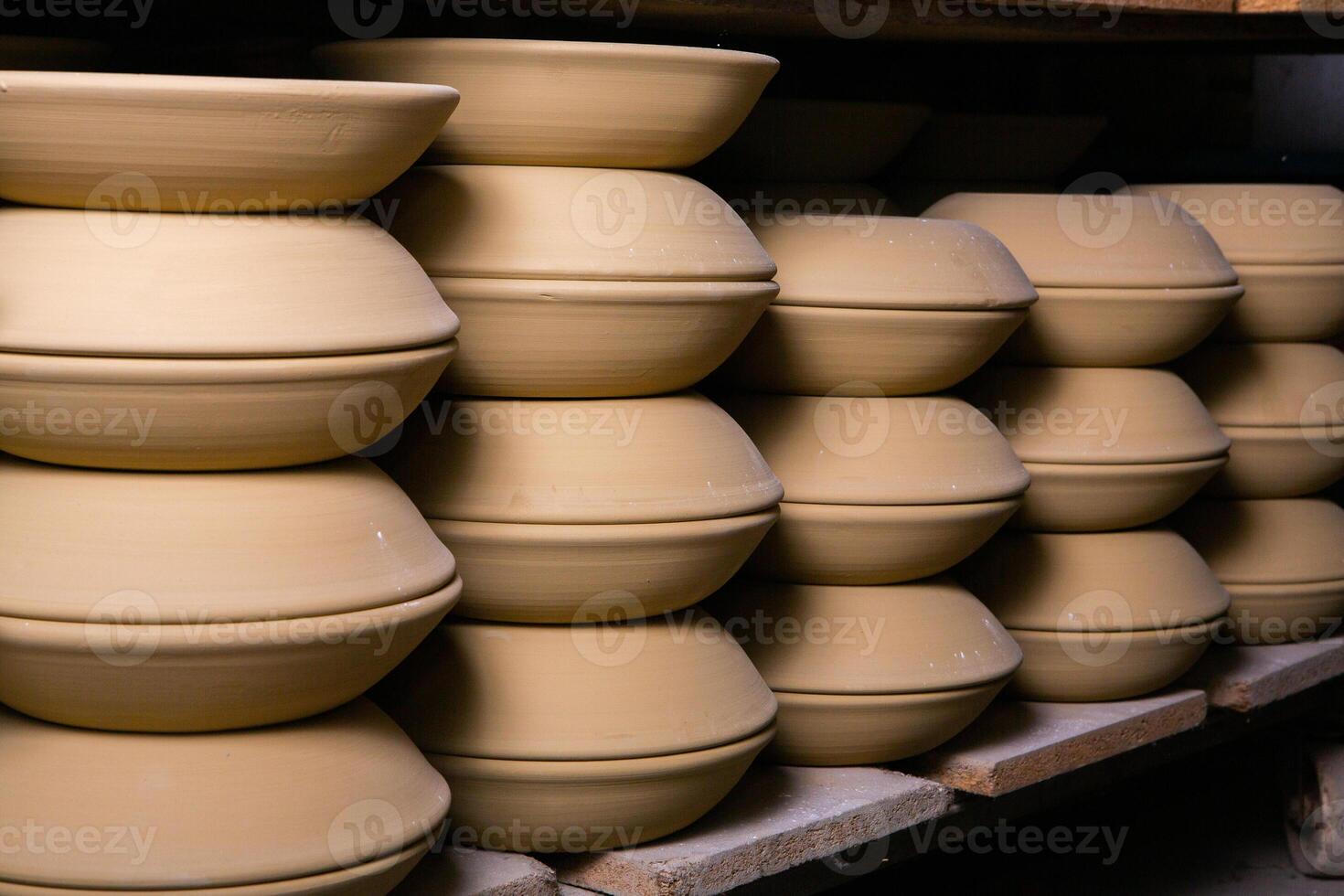 Freshly made clay mugs, pots and bowls drying up on wooden shelves in pottery workshop. Handmade ceramics manufacture. Different clay pots in workshop. photo
