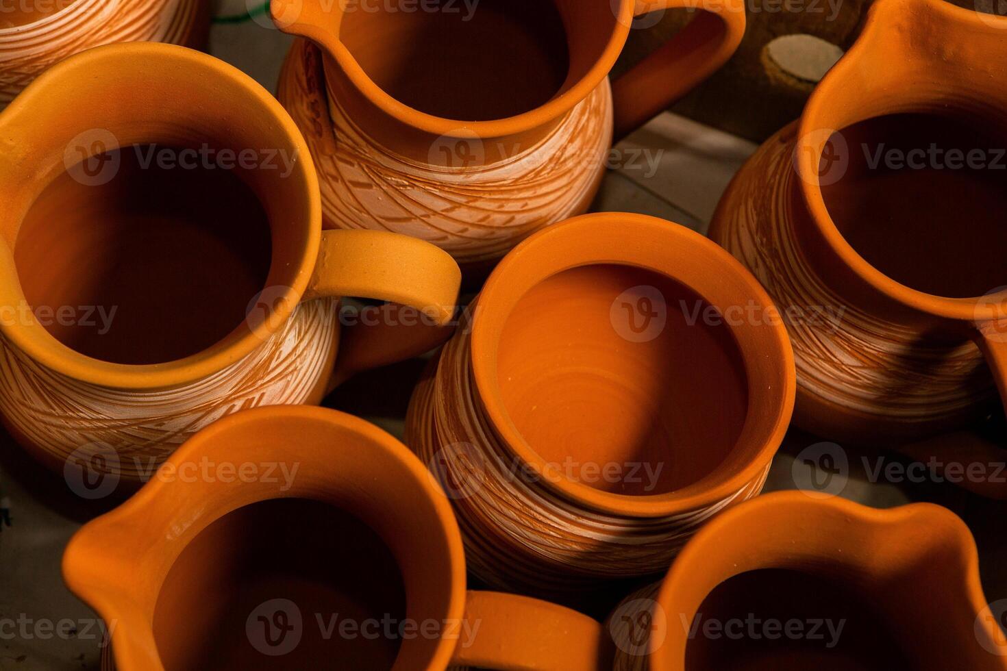 Freshly made clay mugs, pots and bowls drying up on wooden shelves in pottery workshop. Handmade ceramics manufacture. Different clay pots in workshop. photo