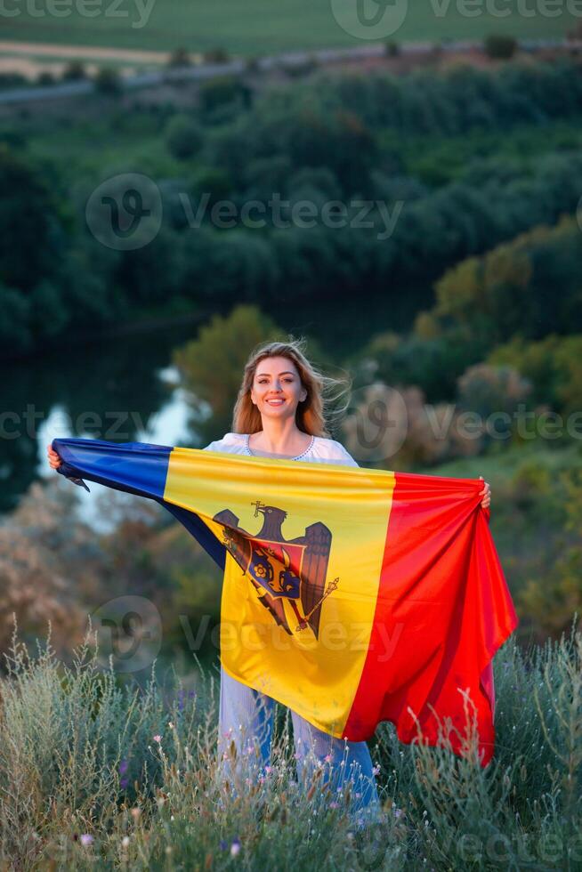 The beautiful lady holding the flag of the Republic of Moldova on a beautiful hill in nature. photo