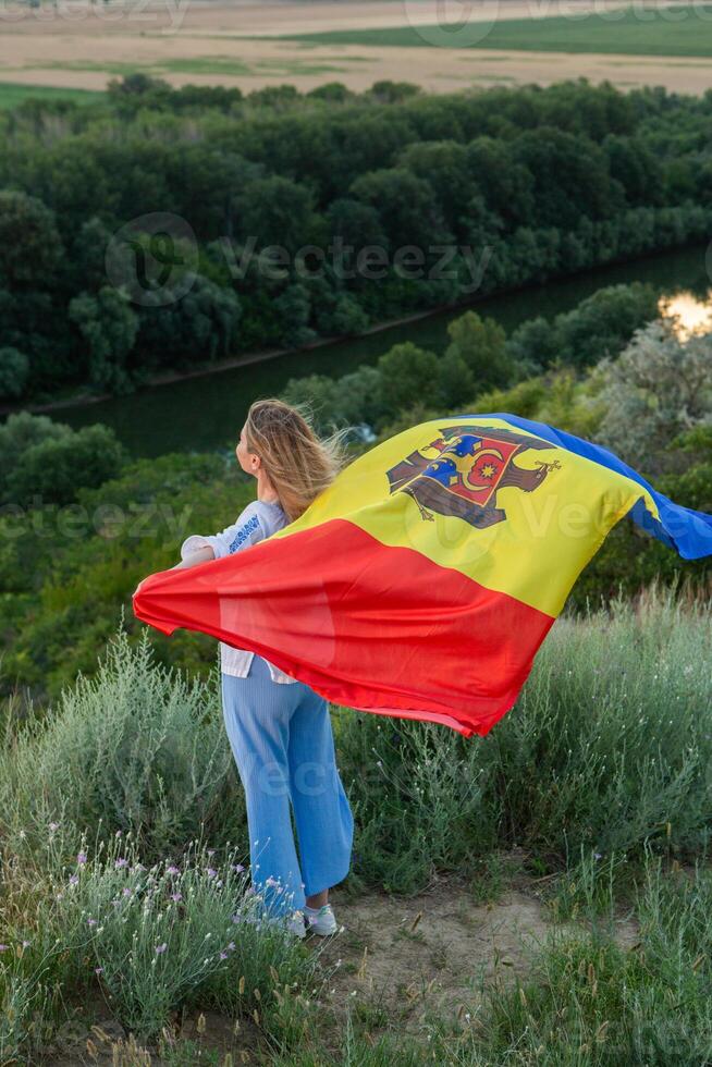 The beautiful lady holding the flag of the Republic of Moldova on a beautiful hill in nature. photo