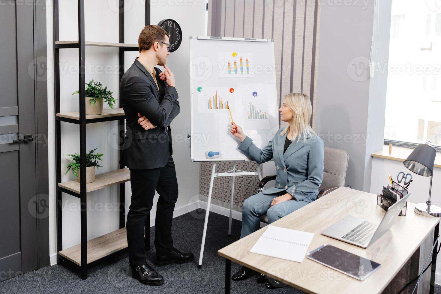 Confident business coach gives presentation on flip chart. A young woman and a man are talking and discussing business project schedules in the office photo