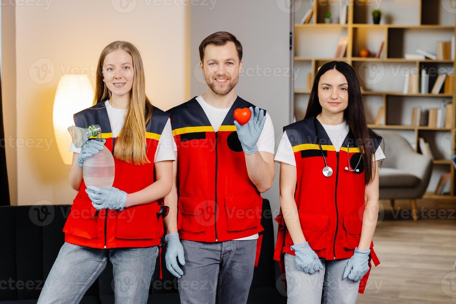 A group of young medical people in uniform stand in the middle of the classroom and smile after a first aid lesson. A man holds a red heart in his hands. Concept of assistance photo