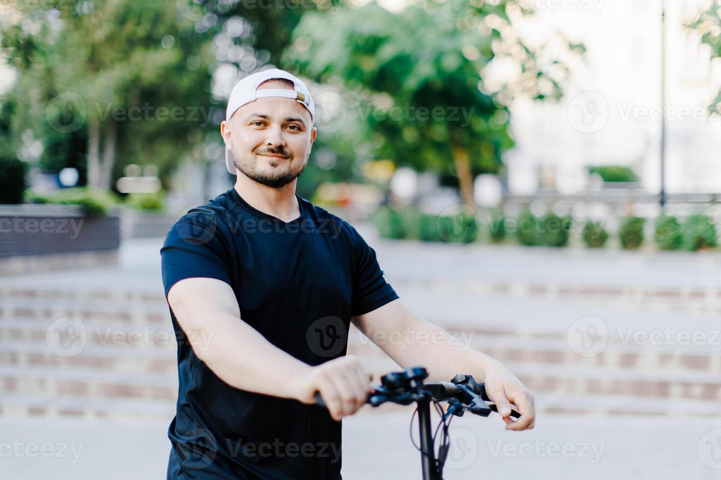 Young handsome man in white baseball cap riding on scooter to work along the street in the city photo