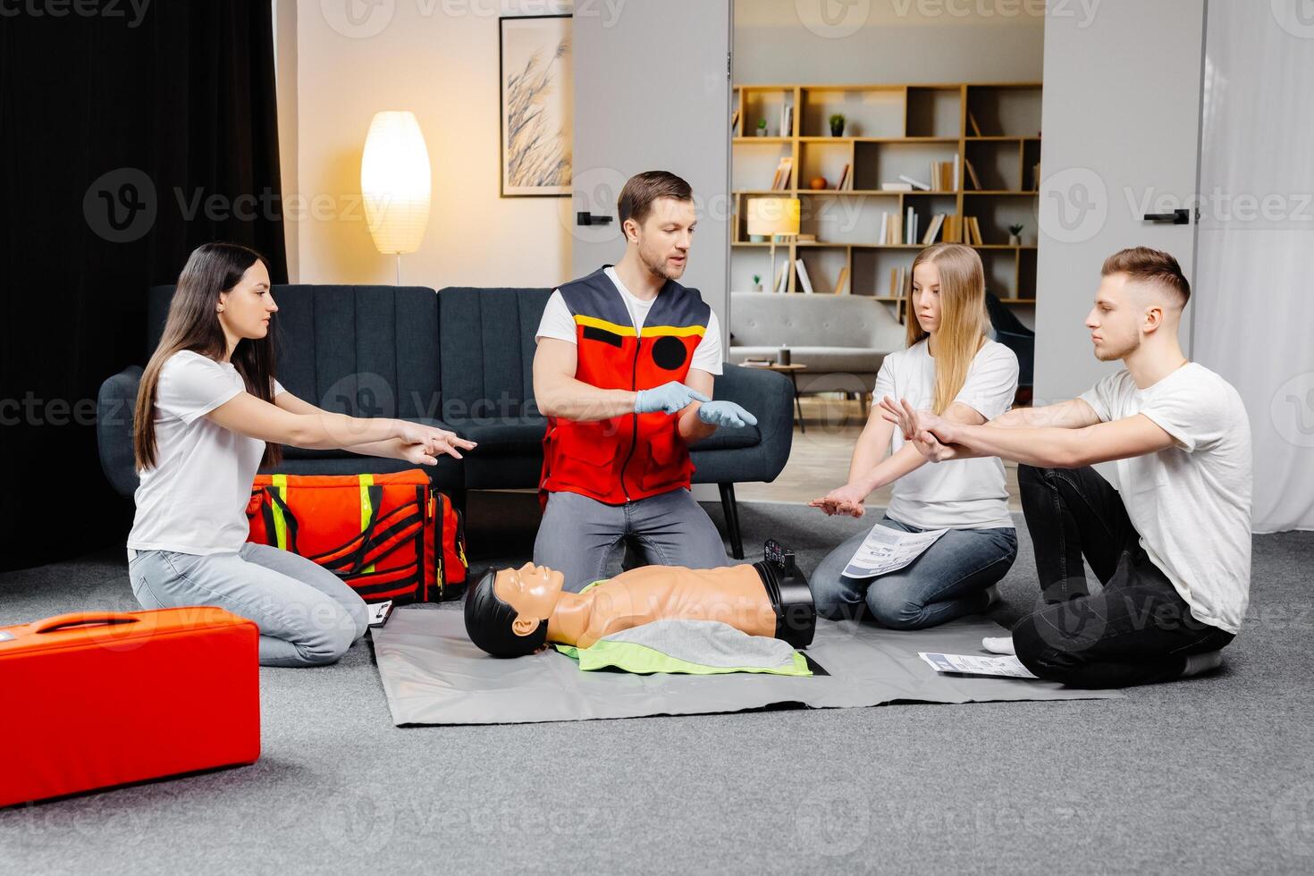 Young man instructor helping to make first aid heart compressions with dummy during the group training indoors photo