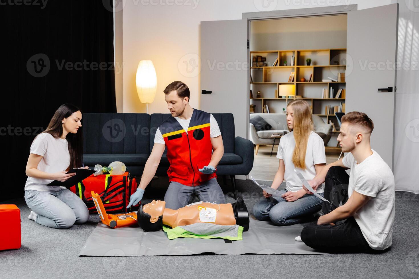 Young man instructor helping to make first aid heart compressions with dummy during the group training indoors photo