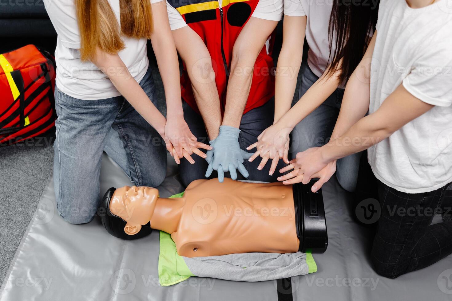 Young man instructor helping to make first aid heart compressions with dummy during the group training indoors photo