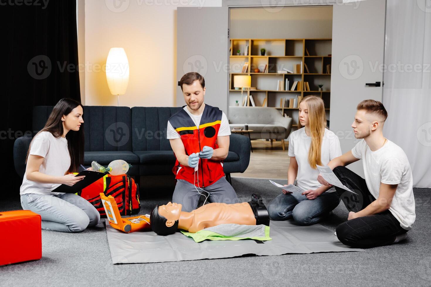 Young man instructor helping to make first aid heart compressions with dummy during the group training indoors photo