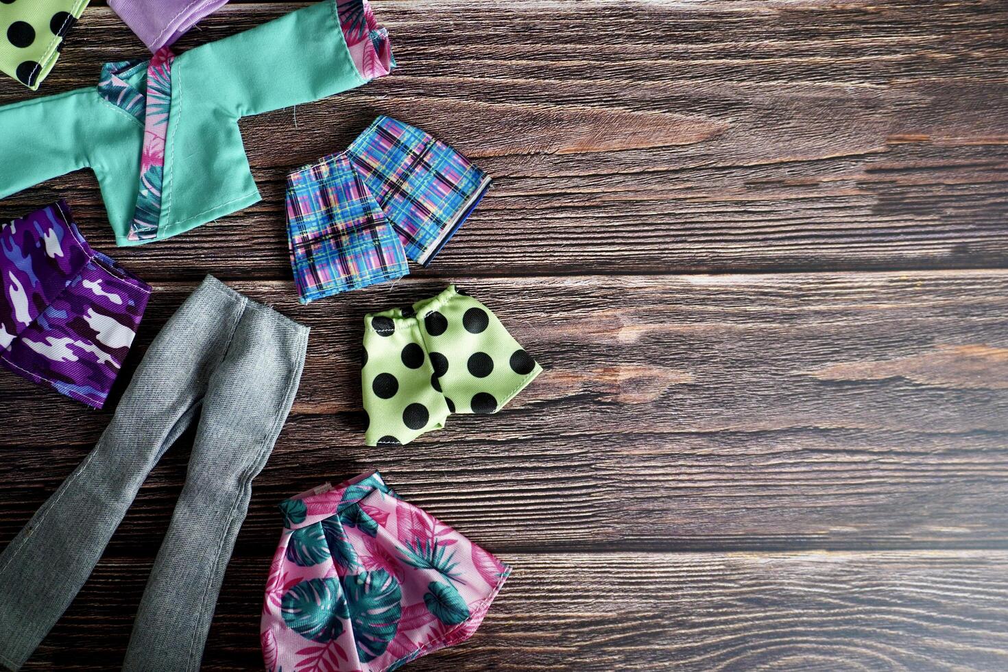 Groups of colorful small human doll fashion clothing object isolated on horizontal ratio empty copy spaced dark wooden surface table top background. photo