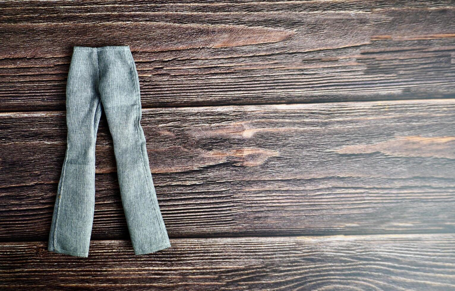 Blue light gray colored denim jeans long pants. Small human doll fashion clothing object isolated on horizontal ratio copy spaced for text dark wooden surface table background. photo