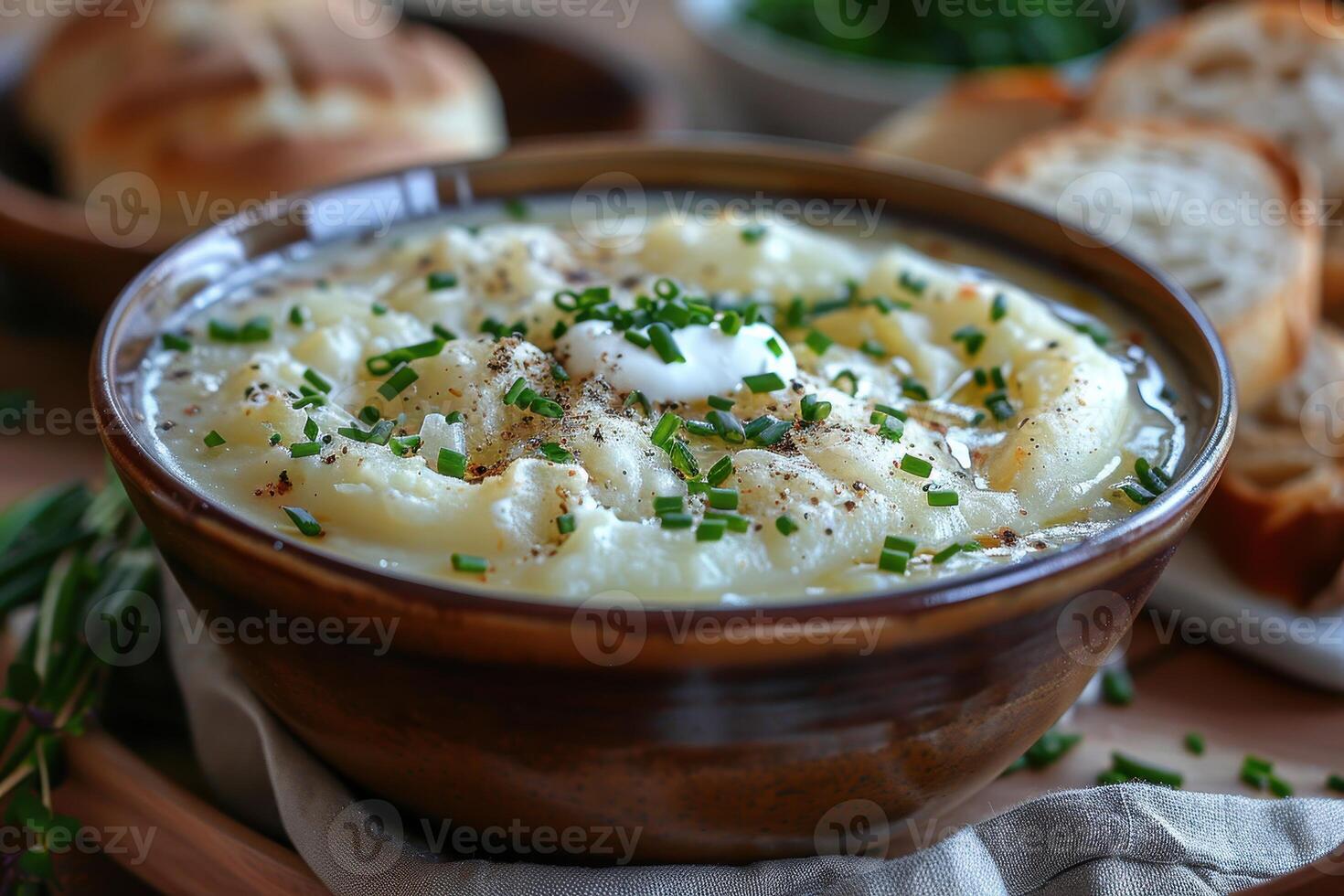 A bowl of creamy leek and potato soup, garnished with chives and a swirl of cream, served with a crusty bread roll. photo