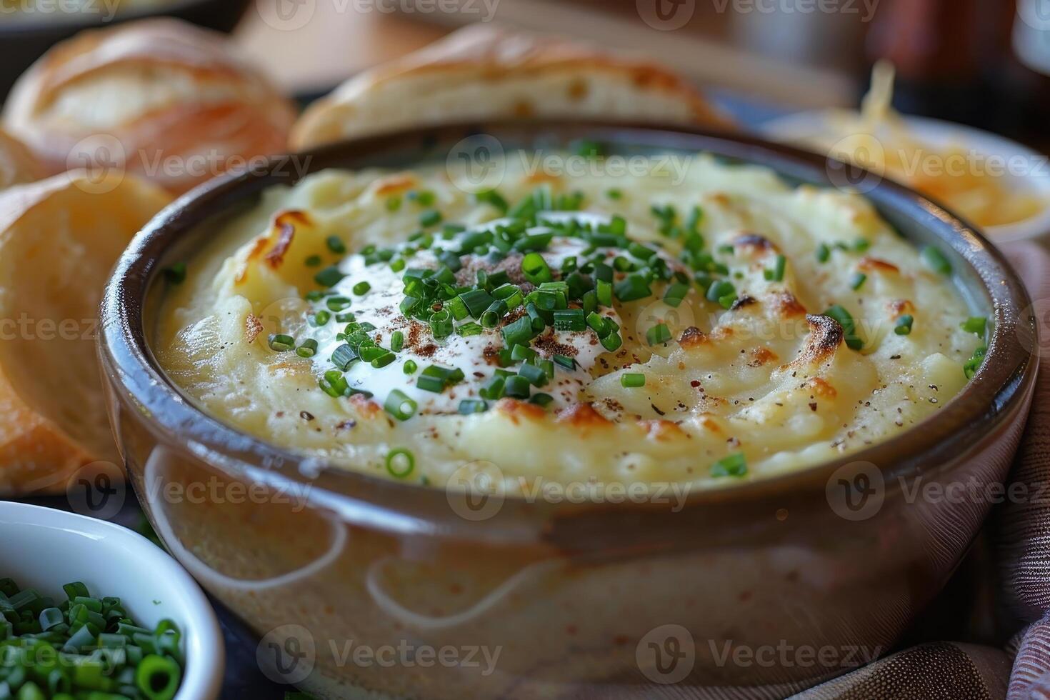 A bowl of creamy leek and potato soup, garnished with chives and a swirl of cream, served with a crusty bread roll. photo