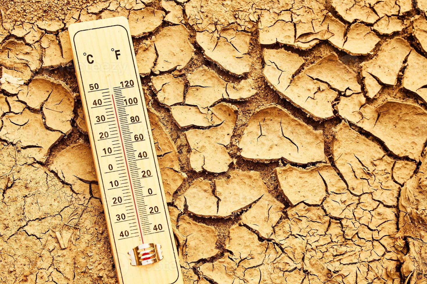Climate change concept. Thermometer on arid, cracked soil representing extreme heat and drought conditions. photo