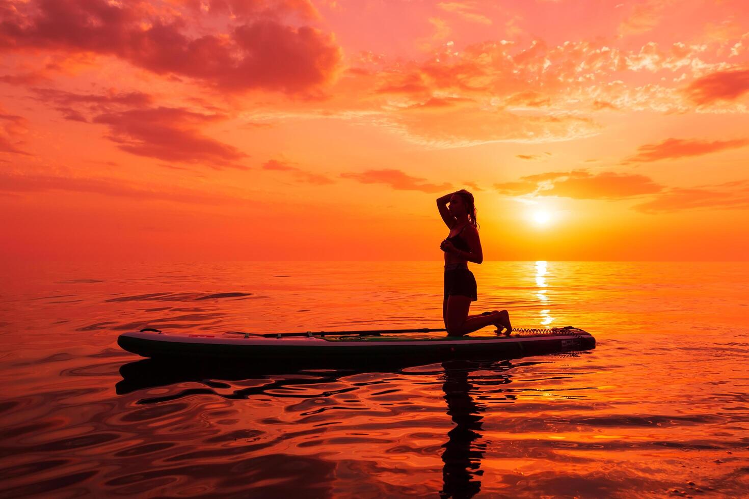 June 25, 2021. Anapa, Russia. Sporty woman relaxing on stand up paddle board at quiet sea with sunset or sunrise. Woman on Red Paddle SUP board and sunset. photo