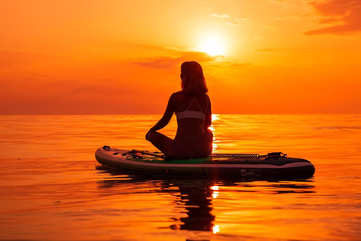 June 25, 2021. Anapa, Russia. Sporty woman sitting on stand up paddle board at sea with sunset or sunrise. Woman on Red Paddle SUP board and sunset. photo