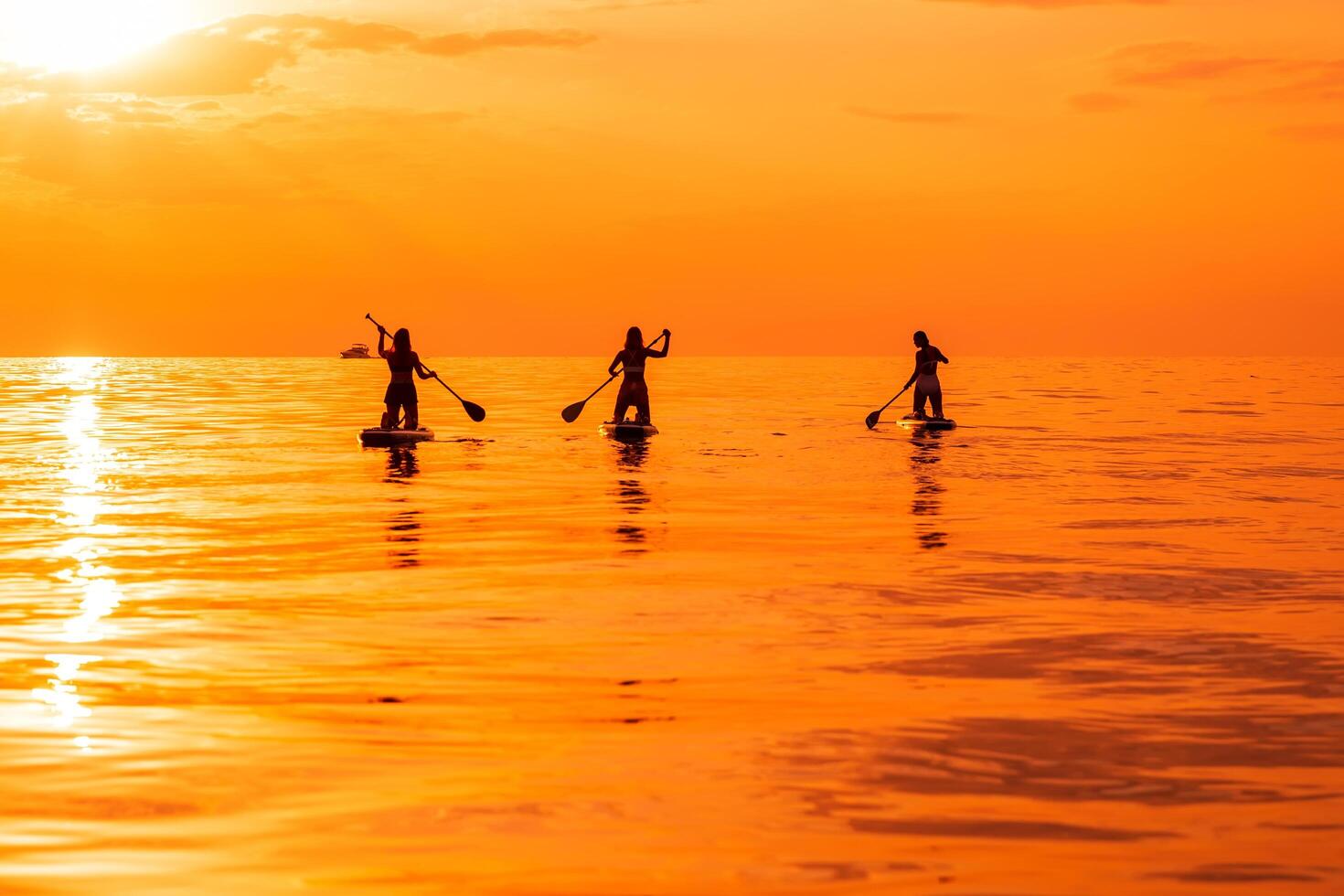 June 25, 2021. Anapa, Russia. Travelers on stand up paddle board at ocean with sunset or sunrise. Girls on Red Paddle sup board and sunset with reflection photo