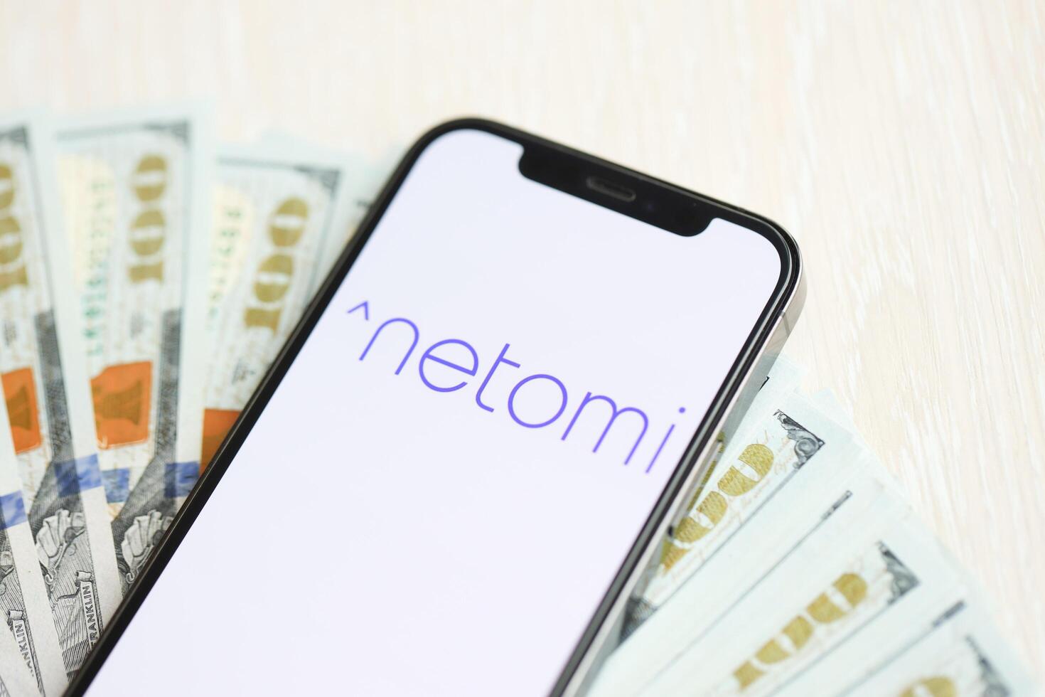KYIV, UKRAINE - MARCH 17, 2024 Netomi logo on iPhone display screen with many hundred dollar bills photo