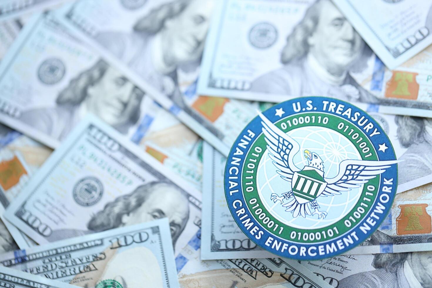 KYIV, UKRAINE - JUNE 26, 2024 U.S. Treasury Financial Crimes Enforcement Network coat of arms on big amount of US dollar banknotes photo