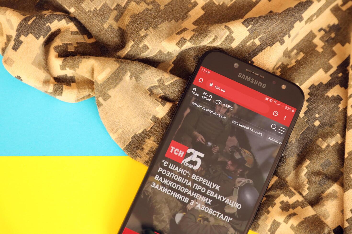 KYIV, UKRAINE - 4 MAY, 2023 TSN ukrainian news portal on smartphone screen with ukrainian flag and camouflage fabric photo