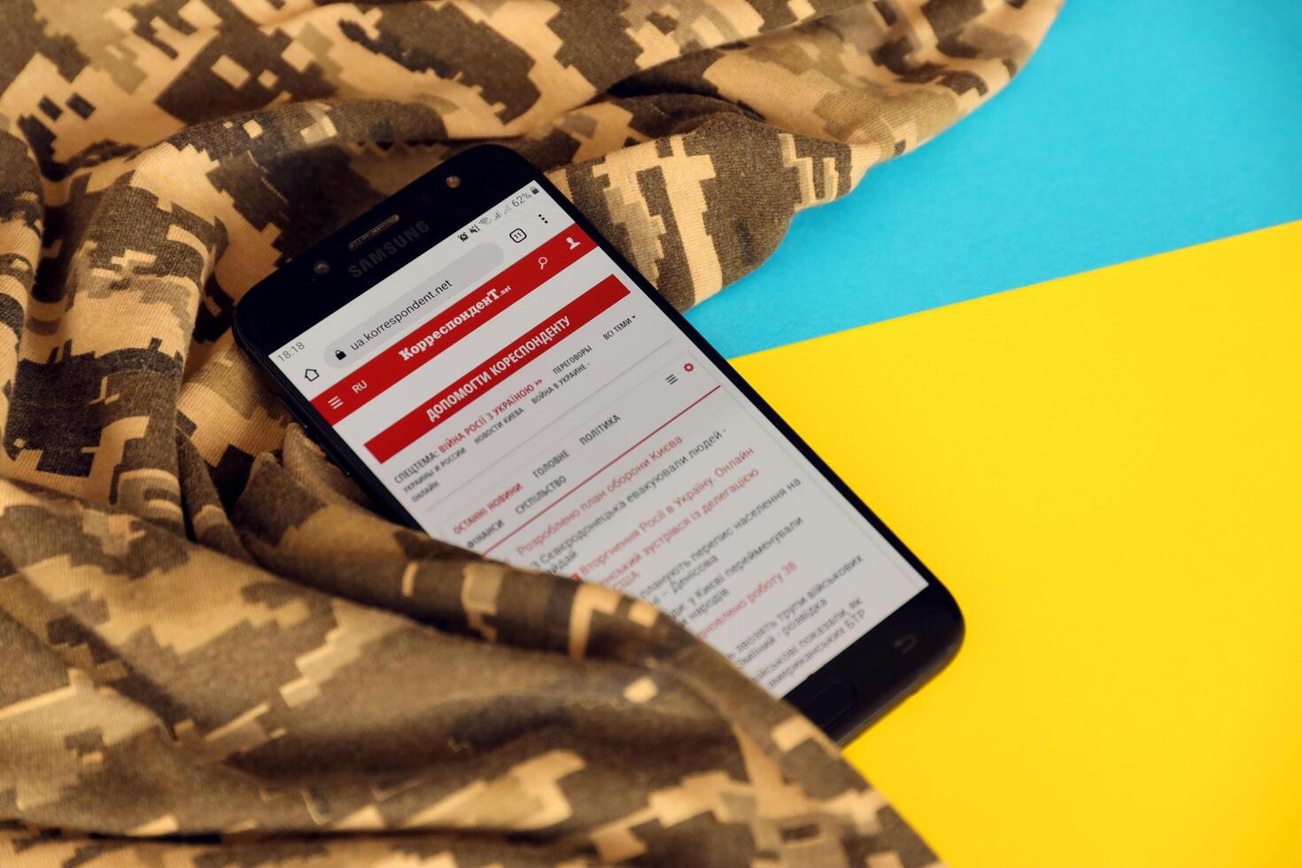 KYIV, UKRAINE - 4 MAY, 2023 Correspondent ukrainian news portal on smartphone screen with ukrainian flag and camouflage fabric photo