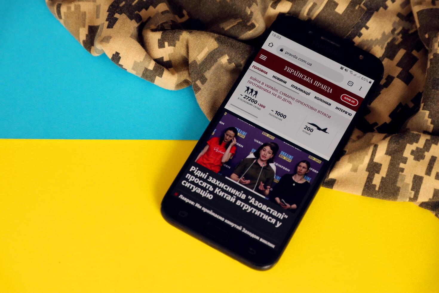 KYIV, UKRAINE - 4 MAY, 2023 UP Ukrainska Pravda ukrainian news portal on smartphone screen with ukrainian flag and camouflage fabric photo