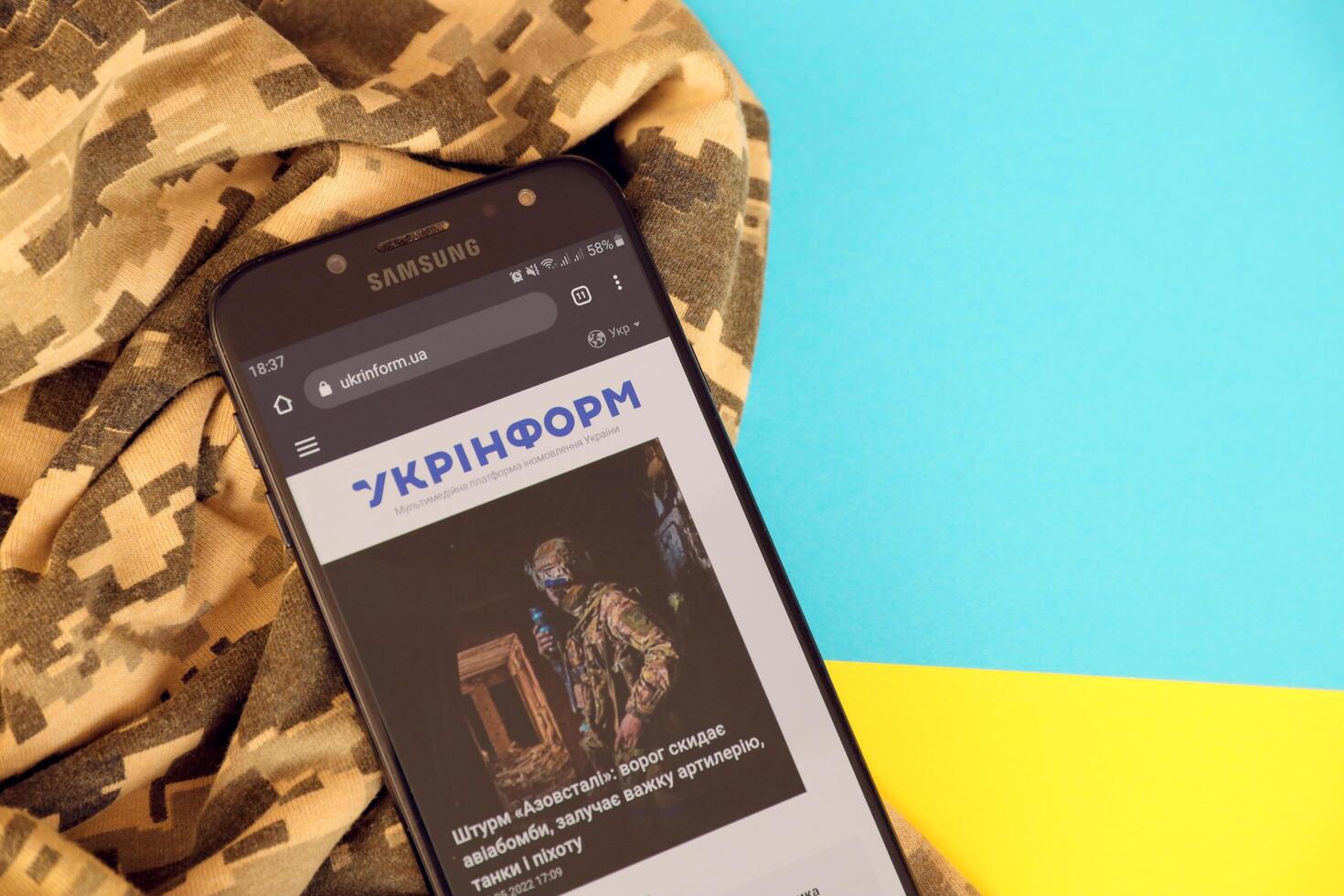KYIV, UKRAINE - 4 MAY, 2023 Ukrinform ukrainian news portal on smartphone screen with ukrainian flag and camouflage fabric photo