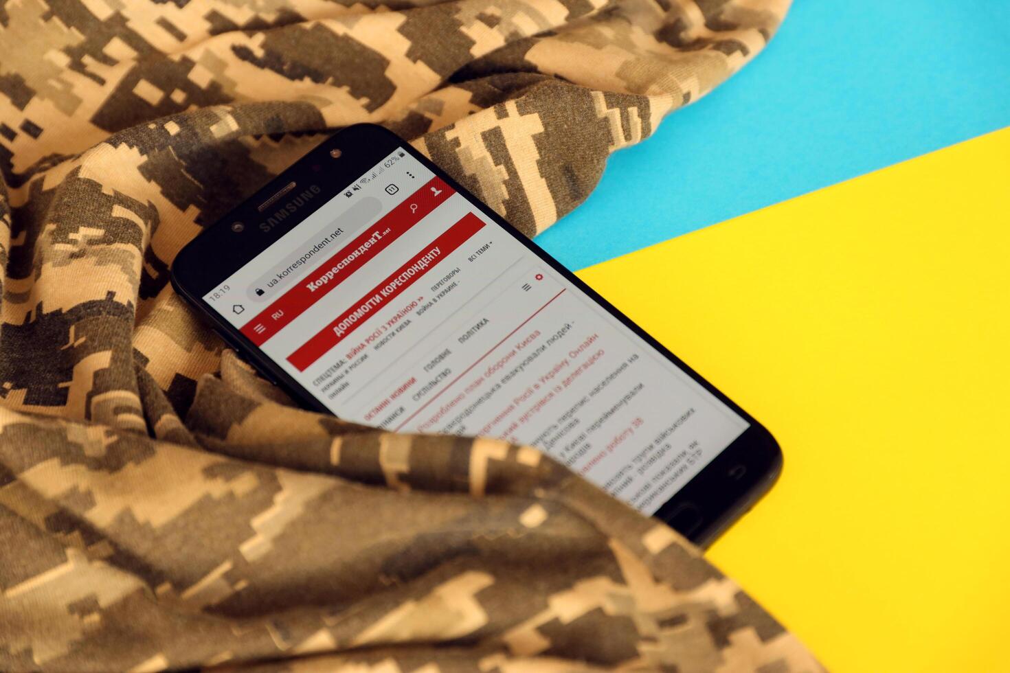 KYIV, UKRAINE - 4 MAY, 2023 Correspondent ukrainian news portal on smartphone screen with ukrainian flag and camouflage fabric photo
