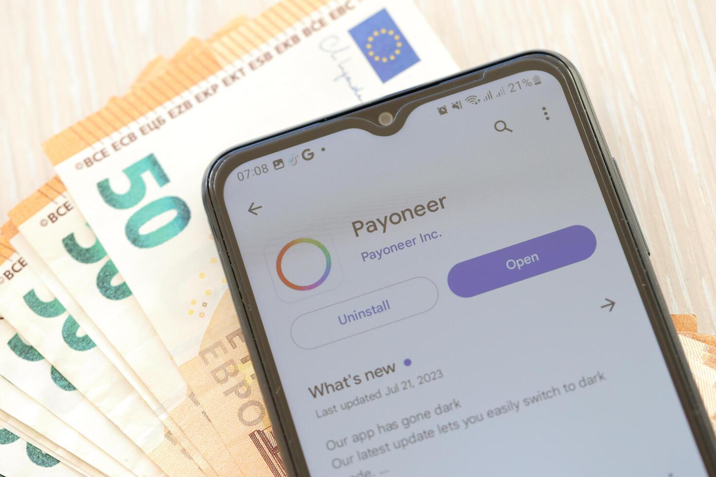 TERNOPIL, UKRAINE - AUGUST 3, 2023 Payoneer application on screen on modern smartphone and many bills of euro currency photo