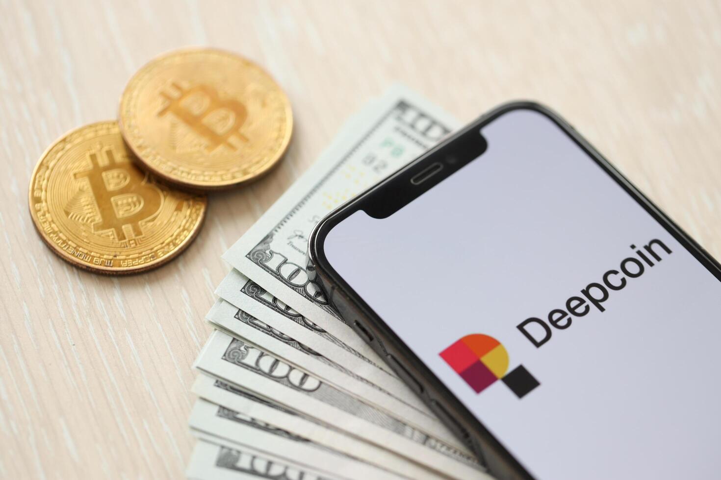 KYIV, UKRAINE - MARCH 15, 2024 Deepcoin logo on iPhone display screen with dollars and bitcoins on table photo