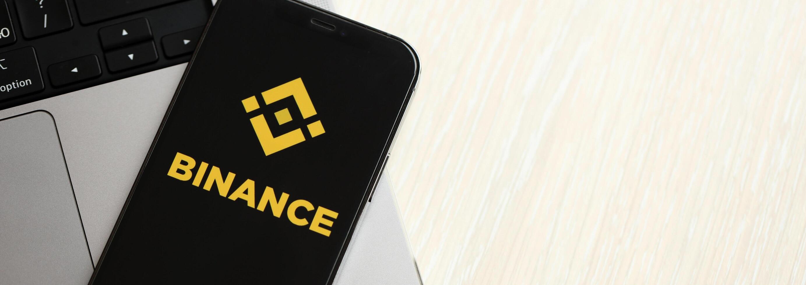 KYIV, UKRAINE - MARCH 15, 2024 Binance logo on iPhone display screen on MacBook panel logo on iPhone display screen with dollars and bitcoins on MacBook photo