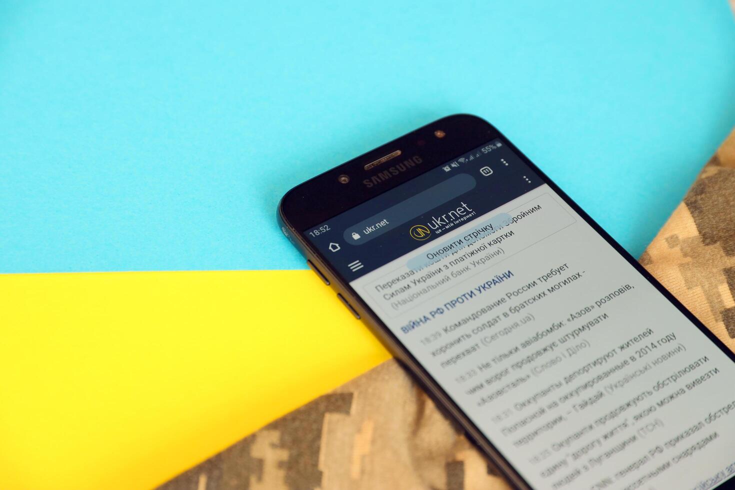 KYIV, UKRAINE - 4 MAY, 2023 Ukr Net ukrainian news portal on smartphone screen with ukrainian flag and camouflage fabric photo