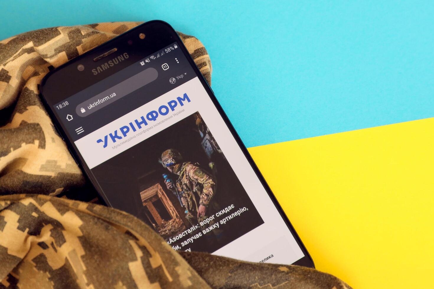 KYIV, UKRAINE - 4 MAY, 2023 Ukrinform ukrainian news portal on smartphone screen with ukrainian flag and camouflage fabric photo
