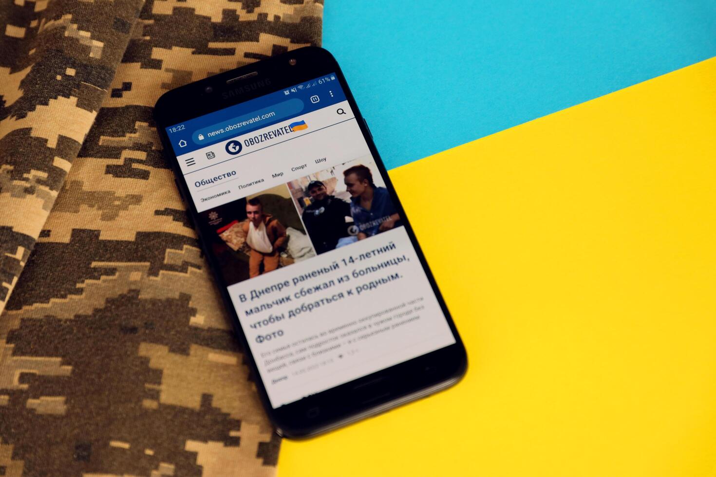 KYIV, UKRAINE - 4 MAY, 2023 Obozrevatel ukrainian news portal on smartphone screen with ukrainian flag and camouflage fabric photo