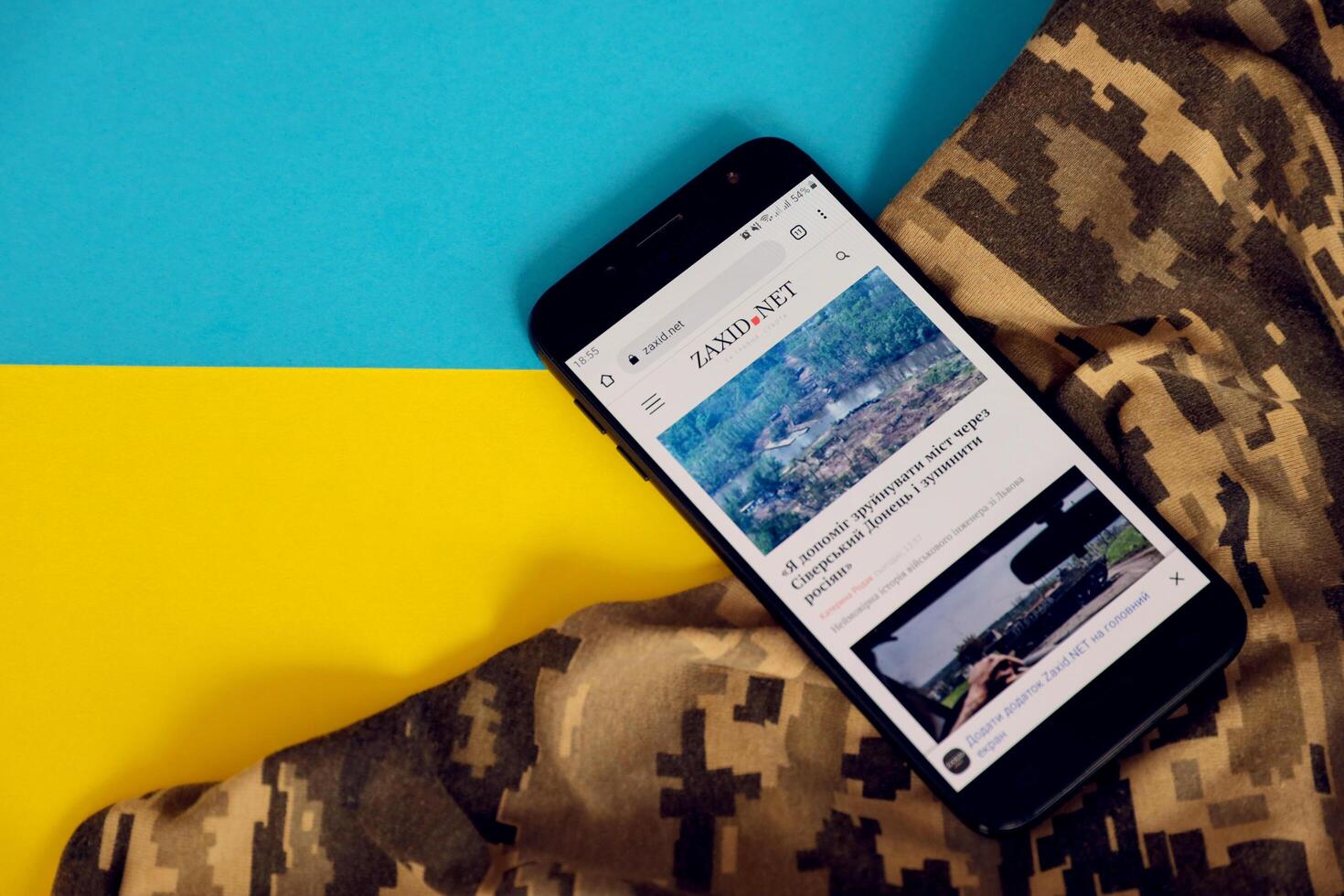 KYIV, UKRAINE - 4 MAY, 2023 Zaxid Net ukrainian news portal on smartphone screen with ukrainian flag and camouflage fabric photo