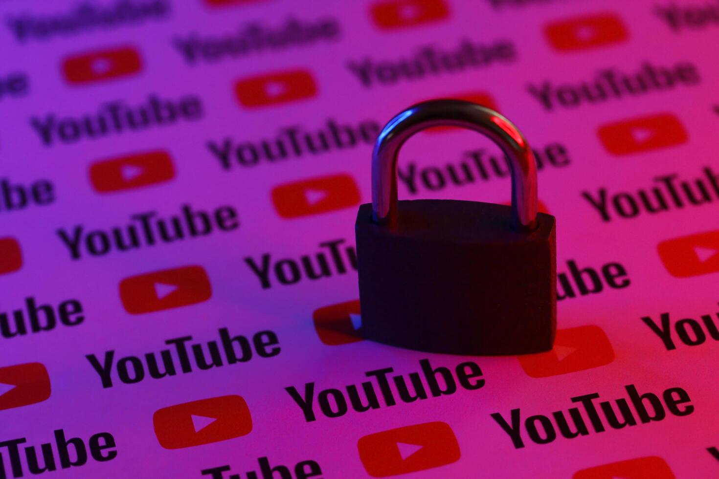 KYIV, UKRAINE - NOVEMBER 27, 2023 Locked small lock on many Youtube logotypes in red and blue light photo