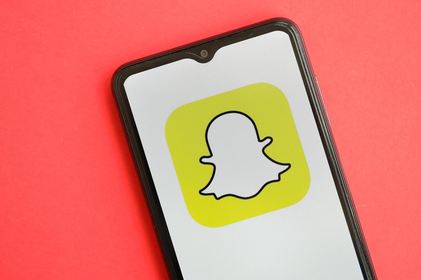 KYIV, UKRAINE - APRIL 1, 2024 Snapchat icon on smartphone screen on red table photo