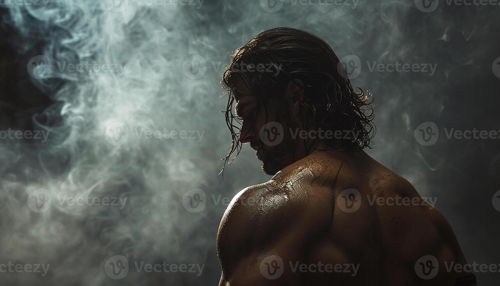 A muscular man is shown in profile with his back to us, his head covered with long hair. The light behind him makes him stand out, In front of him there is smoke outlining the area around his body. photo