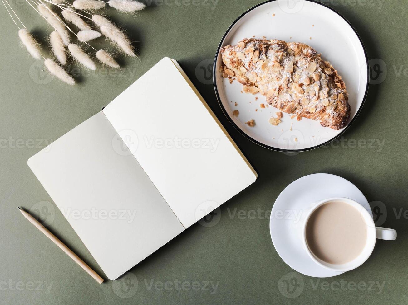 Notebook with blank sheets, cup with coffee, croissant on green background photo